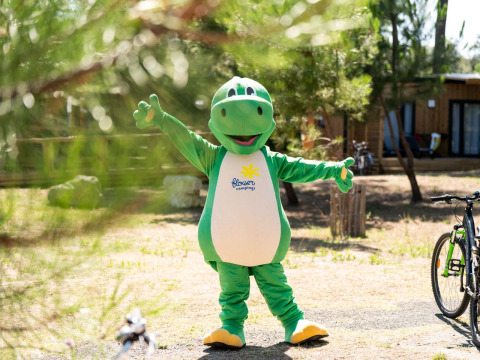 Persona in costume da mascotte dinosauro verde posa all'aperto a Flower Camping Monplaisir, Nouvelle-Aquitaine, Francia.