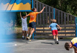 Børn og voksne spiller basketball på udendørs bane på Flower Camping Monplaisir i Nouvelle-Aquitaine, Frankrig.