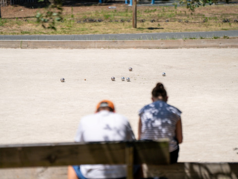 Dos personas sentadas en un banco observan un juego de petanca en Flower Camping Monplaisir, Nouvelle-Aquitaine, Francia.