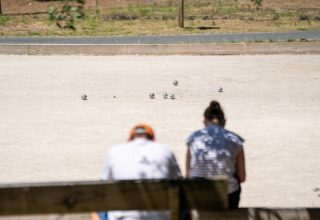 Zwei Personen sitzen auf einer Bank und beobachten ein Pétanque-Spiel im Flower Camping Monplaisir, Frankreich.