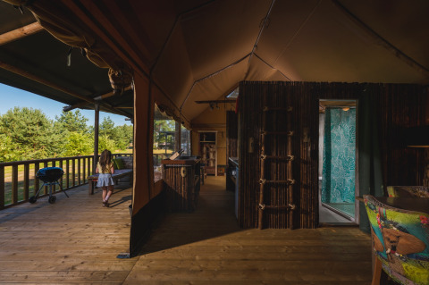Het interieur van een luxe safaritent in Wilsumer Berge, met houten vloer, kind en uitzicht op groen.