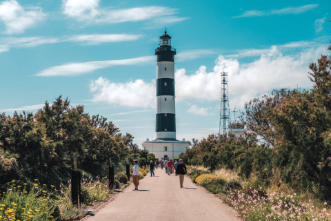 Personas caminando hacia un faro a rayas blancas y negras cerca de Saint-Trojan-les-Bains, Oléron, Francia.
