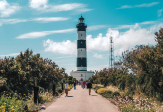 People walk towards a black and white striped lighthouse near Saint-Trojan-les-Bains, Oléron, France.