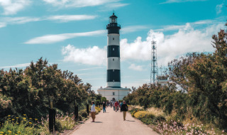 Mennesker går mod en fyrtårn med sorte og hvide striber nær Saint-Trojan-les-Bains, Oléron, Frankrig.