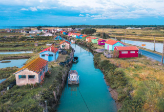 Cabanes colorées et bateaux le long d’un canal au Flower Camping Monplaisir en Nouvelle-Aquitaine, France.
