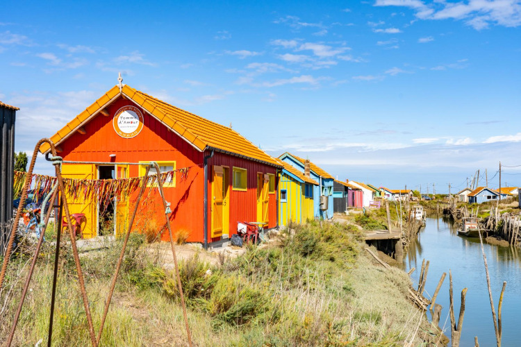 Colorful fishing huts along a canal at Flower Camping Monplaisir in Nouvelle-Aquitaine, France, on a sunny day.