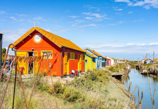 Bunte Fischerhütten am Kanal im Flower Camping Monplaisir, Nouvelle-Aquitaine, Frankreich, an einem sonnigen Tag.