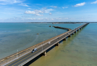 Puente sobre el mar cerca de Flower Camping Monplaisir en Nouvelle-Aquitaine, Francia, con autos y cielo azul.