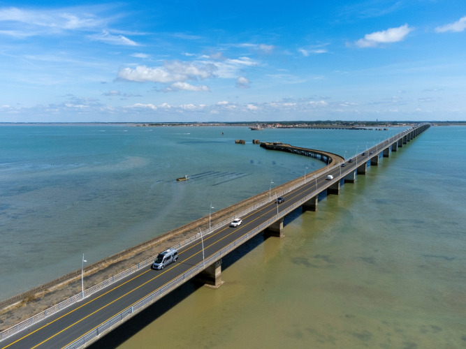Puente sobre el mar cerca de Flower Camping Monplaisir en Nouvelle-Aquitaine, Francia, con autos y cielo azul.