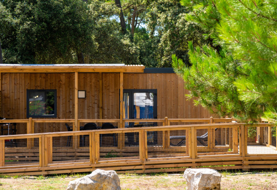 Vue du chalet Premium Stacaravan PRM avec deux chambres, terrasse en bois et environnement verdoyant.