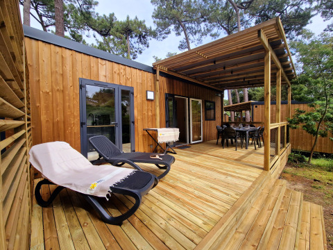 Wooden terrace of Premium Stacaravan with lounge chairs, dining area, and forest surroundings.