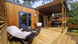 Terrasse der Premium Stacaravan mit Liegestühlen und Essbereich, umgeben von Bäumen und Natur.