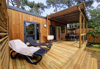 Wooden terrace of Premium Stacaravan with lounge chairs, dining area, and forest surroundings.