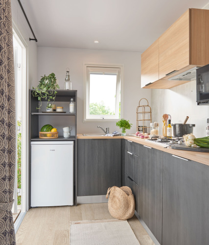 Cocina moderna de cabaña con armarios oscuros, detalles en madera y hierbas frescas junto a la ventana.