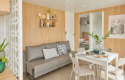 Sala de estar moderna con sofá gris y comedor en una cabaña Premium Stacaravan en Flower Camping Monplaisir.