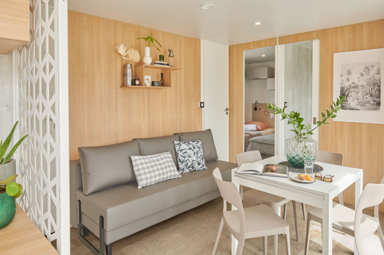 Salon contemporain avec canapé gris, table à manger et déco boisée au Premium Stacaravan de Flower Camping Monplaisir.