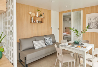 Soggiorno luminoso con divano grigio e tavolo da pranzo in Premium Stacaravan presso Flower Camping Monplaisir.