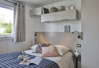 Dormitorio moderno en la Premium Stacaravan de Flower Camping Monplaisir, con cama, ventana y almacenamiento.