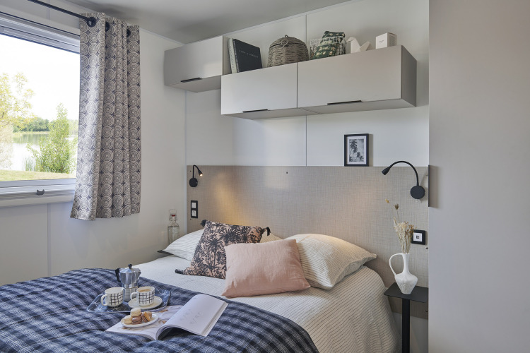 Camera moderna nella Premium Stacaravan al Flower Camping Monplaisir, con letto, armadietti e finestra.