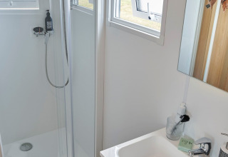 Baño moderno en la Premium Stacaravan con ducha, lavabo, ventanas abiertas y accesorios en Flower Camping Monplaisir.