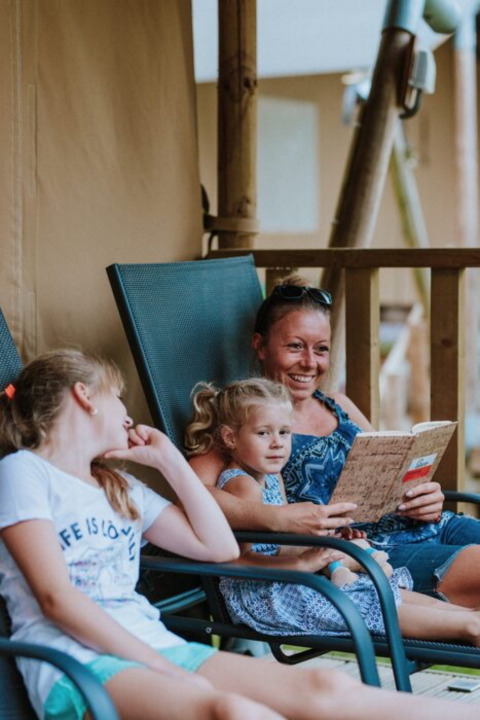 Een moeder leest een boek voor aan haar twee dochters terwijl ze ontspannen op stoelen bij Wilsumer Berge zitten.