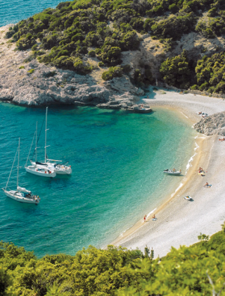 Smuk bugt nær Pomer i Istrien, Kroatien, med turkisblåt vand, sejlbåde og en fredelig strand omgivet af skov.
