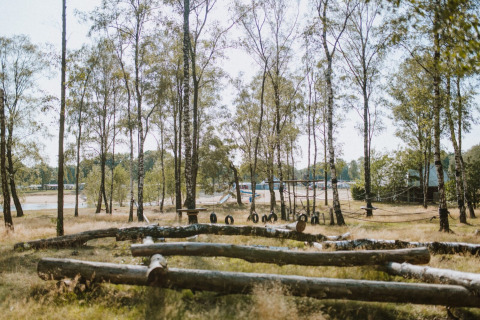 Natuurlijke speeltuin met boomstammen en banden in vakantiepark Wilsumer Berge, Duitsland, omgeven door bomen.