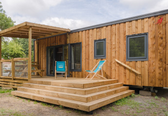 Afbeelding van een moderne houten lodge met terras, strandstoelen en trappen in een groene omgeving.