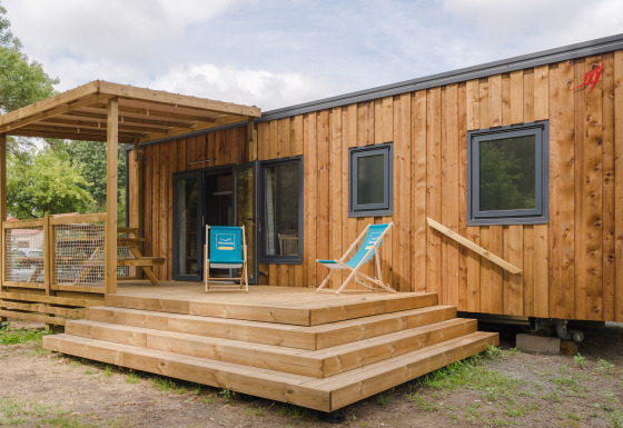 Foto di un lodge moderno in legno con veranda, sedie a sdraio e gradini immerso nella natura verde.