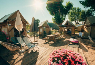 Sonniges Campinggelände mit Holzhütten, Blumen, Sonnenschirmen und Lounge-Stühlen in Lombardo, Italien.