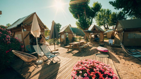 Zonnig buitenterras met tenten, bloembakken, ligstoelen en parasols bij Sivinos Camping Boutique in Lombardije.