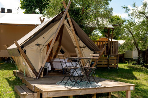 Gezellige glampingtent op houten terras bij Sivinos Camping Boutique in Lombardije, Italië, tussen het groen.
