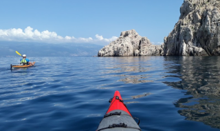 Kajakroning nær klipper og blåt hav ved Njivice, Kroatien, med klar himmel og fredelige omgivelser.