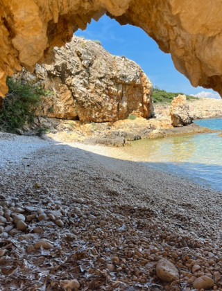 Udsigt fra en kystklippehule i Njivice, Kroatien, der viser stenstrand og klart blåt havvand.