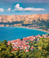 Kystudsigt nær Njivice, Kroatien, med farverige tage, frodig natur og dramatiske bakker i baggrunden.