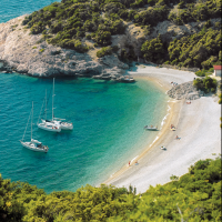 Smuk bugt nær Njivice, Kroatien, med sejlbåde i klart blåt vand og en fredelig strand omgivet af grønne bakker.