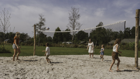 Famiglia che gioca a beach volley vicino a una tiny house al Camping Si-Es-An nei Paesi Bassi.