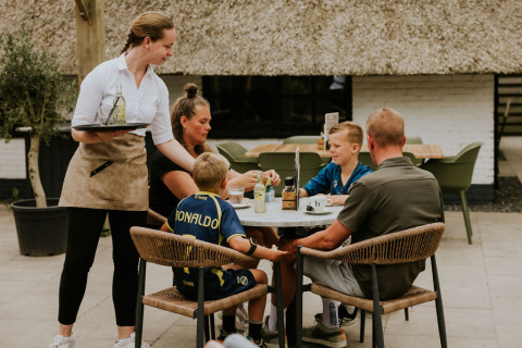 En familie sidder ved et bord udenfor Cosy house på Camping Si-Es-An i Holland og bliver serveret.
