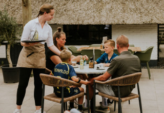 Una familia come al aire libre en la Cosy house de Camping Si-Es-An, Países Bajos, atendida por una camarera.