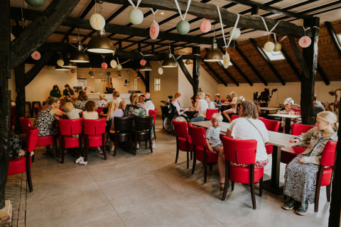 Persone sedute ai tavoli all'interno di Cosy house al Camping Si-Es-An nei Paesi Bassi, con decorazioni.