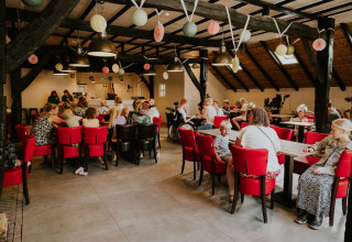 Persone sedute ai tavoli all'interno di Cosy house al Camping Si-Es-An nei Paesi Bassi, con decorazioni.