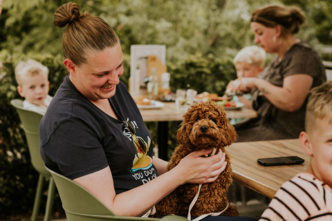 En kvinde smiler og holder en brun hund på skødet udenfor ved et bord med familie på Cosy House, Camping Si-Es-An.