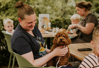 Una mujer sonríe sosteniendo un perro marrón en su regazo al aire libre con familia en Cosy House, Camping Si-Es-An.