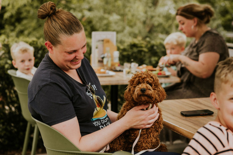Una mujer sonríe sosteniendo un perro marrón en su regazo al aire libre con familia en Cosy House, Camping Si-Es-An.