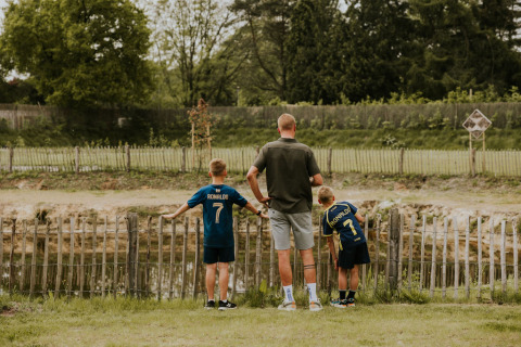 Man and two boys in Ronaldo jerseys stand by a fence near water at Camping Si-Es-An in the Netherlands.
