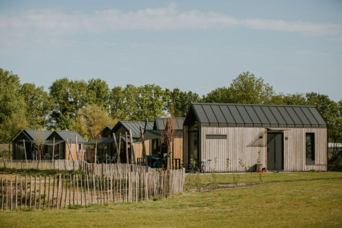 En række små træhytter på Camping Si-Es-An i Holland, omgivet af grønt græs og træer.