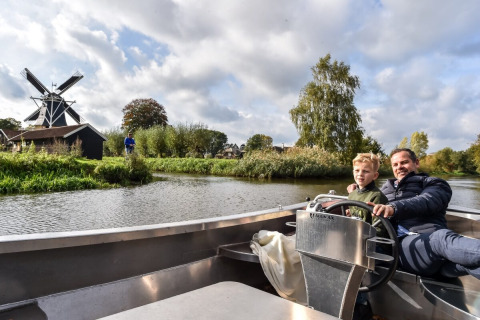 Vader en zoon varen in een boot op een rivier bij een windmolen, Vakantiepark Hölte, Overijssel, Nederland.
