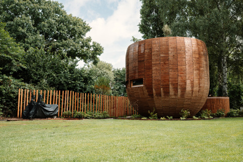 Round wooden tiny house called The Nutshell with fence, lawn and trees at Recreation Park Den Blanken.