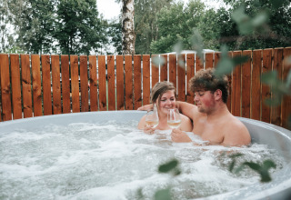 Koppel ontspant met wijn in een hot tub bij The Nutshell, Recreatiepark Den Blanken, Nederland.