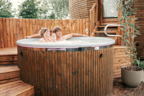 A couple relaxes in a hot tub at The Nutshell tiny house with sauna at Recreation Park Den Blanken, Netherlands.